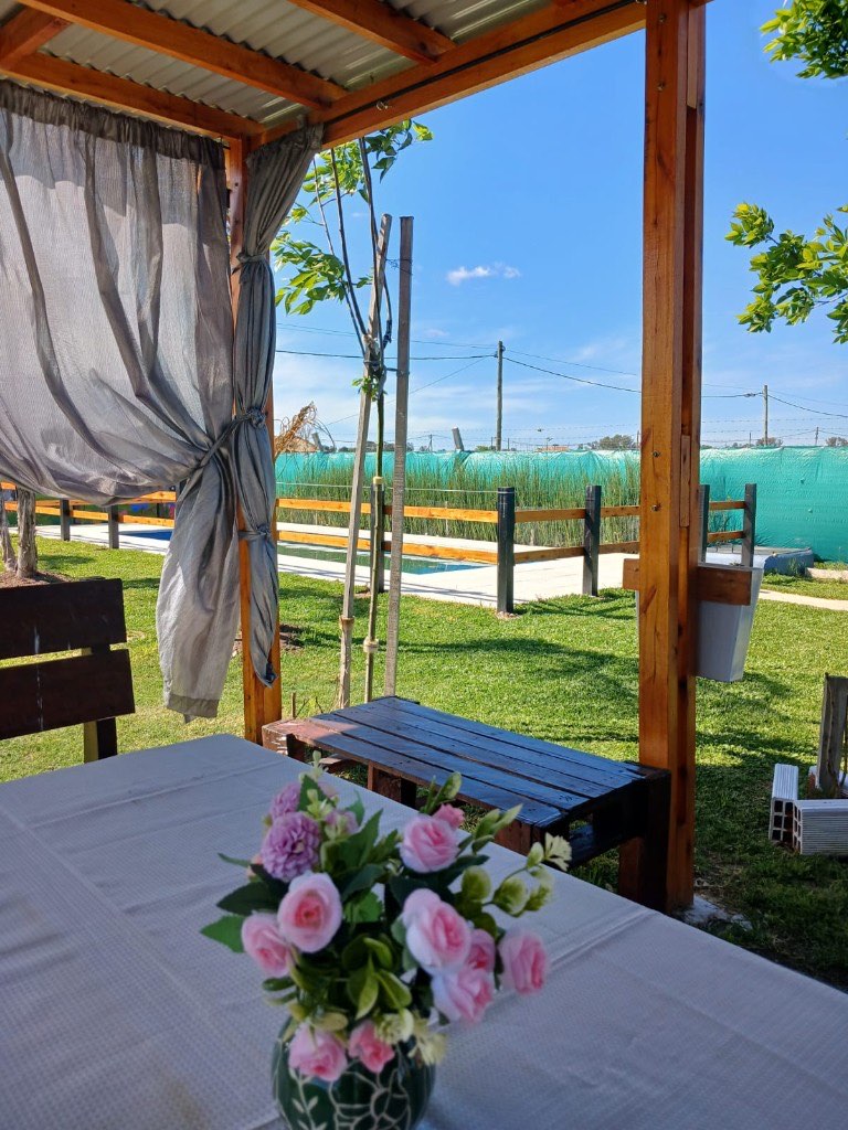 Mesa del quincho con flores, pileta y parque de fondo
