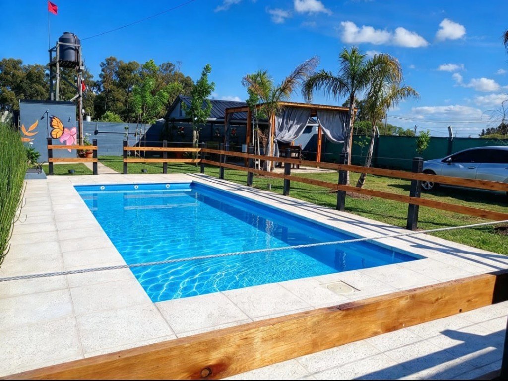 Vista de la quinta en Guernica: pileta rectangular, parque, cerco de madera y pérgola